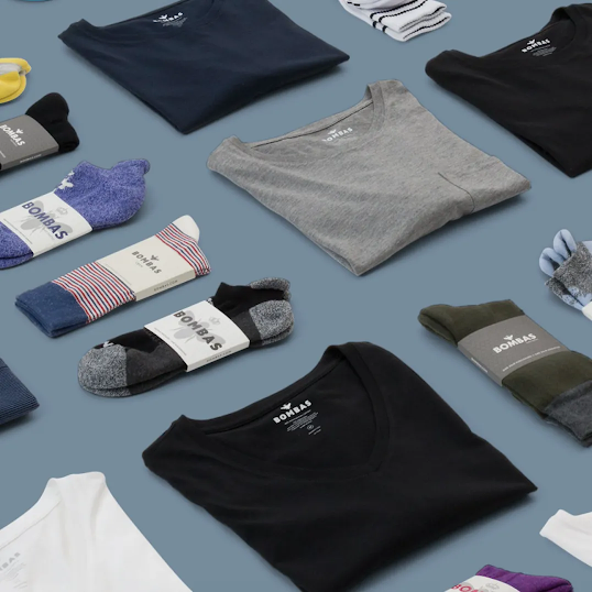 Mehrere Produkte von Bombas, z. B. T-Shirts und Strümpfe, liegen ordentlich gefaltet und in gleichem Abstand zueinander auf einer blauen Fläche.